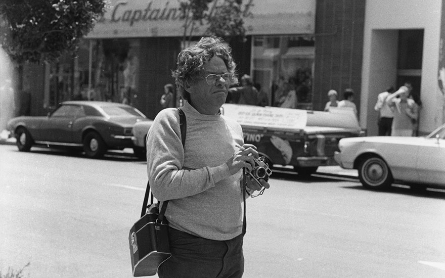 Garry Winogrand studying the scene, with his camera on his hands.